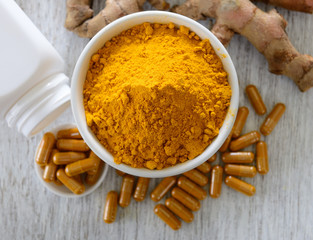 Turmeric powder and turmeric capsules on wooden background