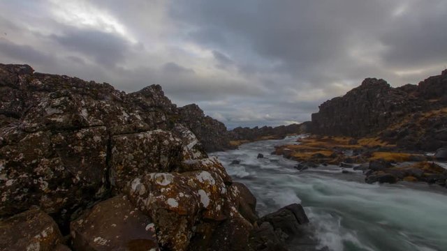 A stationary time-lapse of Pingviller Waterfall in Iceland. A dark and moody landscape with fast moving clouds and mist from the waterfall coming into frame.