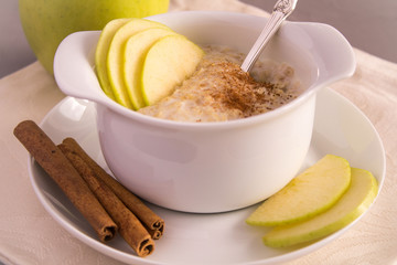 Fasty oatmeal with milk, green apple and cinnamon in the white plate