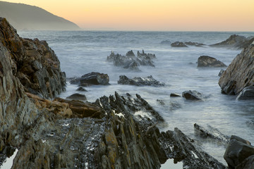 Fototapeta na wymiar Landscape view of a rocky channel at the mouth of the Storms River in the Tsitsikamma Nature Reserve in South Africa. A long exposure smoothes the water in this photograph.