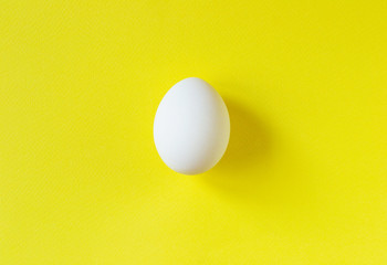 Single white egg on vibrant yellow background