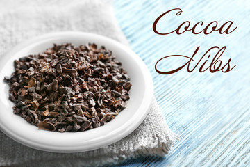 Saucer of aromatic cocoa nibs with napkin and text on wooden background