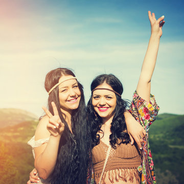 Two boho women smiling gesturing peace