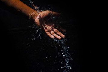 Fototapeta na wymiar Human Hand Capturing The Water That Is Flowing With Motion Blur Effect Over Black Background
