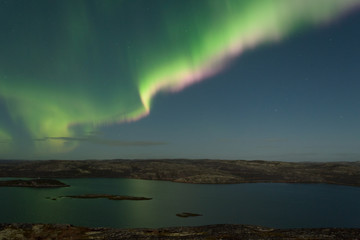 The Aurora in the sky above the hills and water on a moonlit night.
