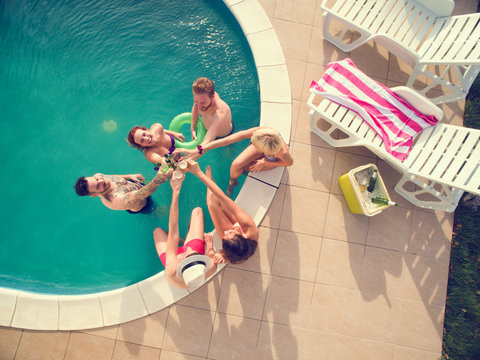 Top view of young girls and boys in swimming pool toasting with bear