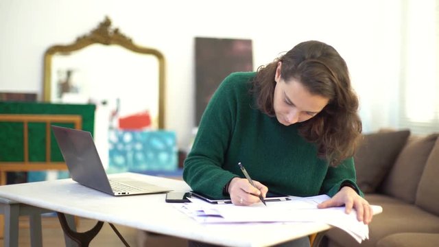 Young woman consulting laptop computer while drawing on paper