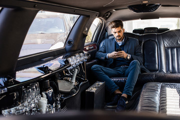 Young business man in limo typing on smart phone - obrazy, fototapety, plakaty
