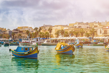 Marsaxlokk, Malta - Traditional colorful maltese Luzzu fisherboats at the old village of Marsaxlokk with turquoise sea water and palm trees on a summer day