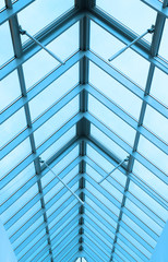 A view through a triangular arched glass roof to the overcast sky, white aluminum frames, double-glazed windows. Photo partially toned 
