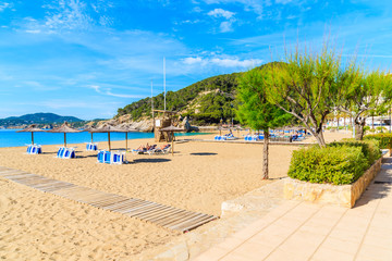 Sandy beach with umbrellas and sunbeds in Cala San Vicente bay on sunny summer day, Ibiza island, Spain