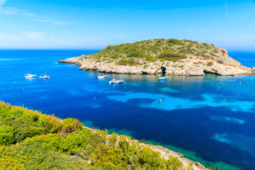 Green coast and view of fishing boats on sea in Cala Portinatx bay, Ibiza island, Spain