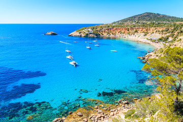 Fototapeta na wymiar Sailing boats on Cala d'Hort bay with beautiful azure blue sea water, Ibiza island, Spain