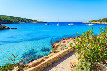 View of coastal promenade along blue sea in Cala Portinatx bay, Ibiza island, Spain