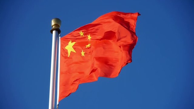 Chinese red flag flutters in wind & blue sky.