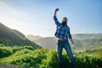 Fototapeta premium excited man with beard and sunglasses cheering in front of grassy green hills in california