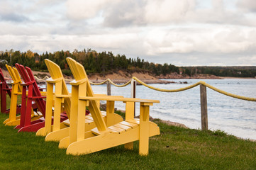 a row of yellow and red adironack chair overlooking water