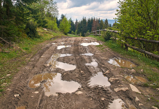 Broken country dirt road in spring mountains with lots of muddy puddles after the rain