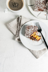 Australian food. Traditional dessert Lamington - pieces of biscuit in dark chocolate, sprinkled with coconut powder chips. On a marble plate, white table. With coffee mug. Copy space top view