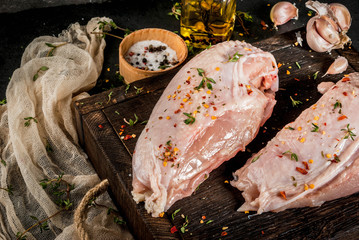 Preparation of food, lunch. Meat. Chicken fillet with skin, raw. On a cutting board, with spices, thyme, garlic, olive oil, salt, pepper. Wooden board, black stone background. Copy space