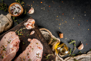 Preparation of food, lunch. Meat. Chicken fillet with skin, raw. On a cutting board, with spices, thyme, garlic, olive oil, salt, pepper. Wooden board, black stone background. Copy space top view