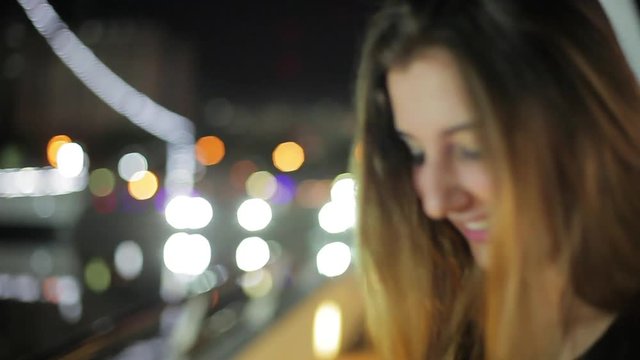 Teenage girl looking at city lights and then smiling at camera at night