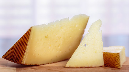 Slices of Manchego curado cheese over a wooden table, in front of a window