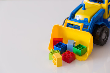 Fototapeta premium Closeup of children toy tractor with colorful plastic bricks or details on white background. Baby's toys on the table isolated.