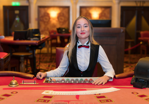 Woman croupier near card table in casino offers to play black jack or  preference and try luck in Las Vegas. Croupier girl in elite poker club or  casino helps to enjoy gambling