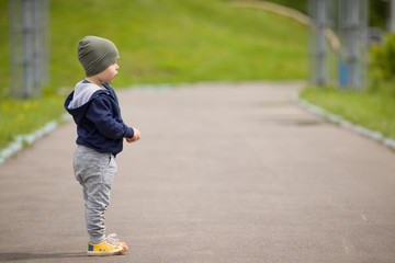 Fototapeta premium Portrait of cute little toddler boy standing on asphalt road and looking in the distance. Child walking outdoors.