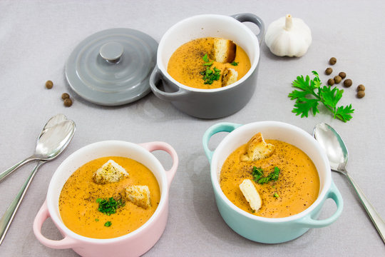 Three small serving pots or bowls with cream soup made of red lentils with rusks, spices and herbs parsley, coriander. On a light gray background.