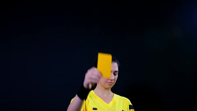 Woman football soccer referee shows penalty yellow card on black background, 4k