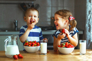 Happy children brother and sister eating strawberries with milk