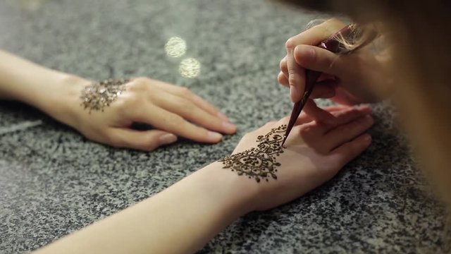 Woman making floral mehendi on a hand with henna on a table.