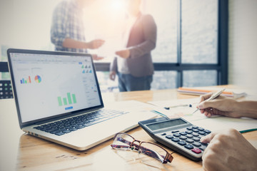 Business people present turnover graph chart paper and doing calculator math for CEO of company with morning light. business partner working blurred background.