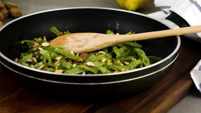 Green beans with roasted almonds on fry pan on kitchen countertop. Slide from right.