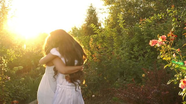 Two sisters in white dresses hug each other in the garden after a long separation. Happiness of a family meeting.
