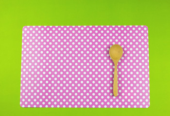 Wooden spoon put on a white polka dots pink place Mat on green background.