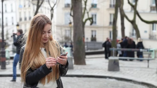 young woman using mobile phone on the street to write sms and check email, caucasian girl looking at the screen of her smartphone