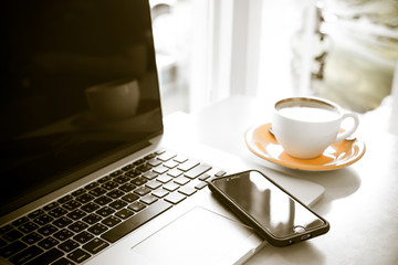 Cup of coffee and smart devices on the table close up. (Processed in vintage colour tone)
