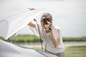 young woman checking under the hood and calling help with smart phone.