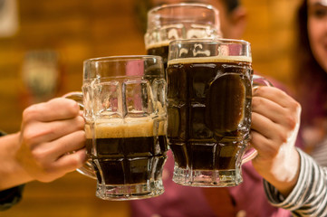 Close up of a happy male friends clinking with beer mugs in pub