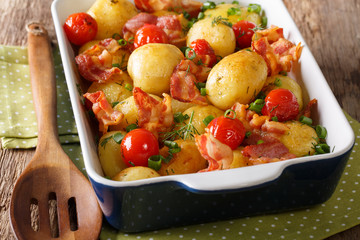 Delicious new potatoes baked with bacon, herbs and tomatoes close-up. horizontal