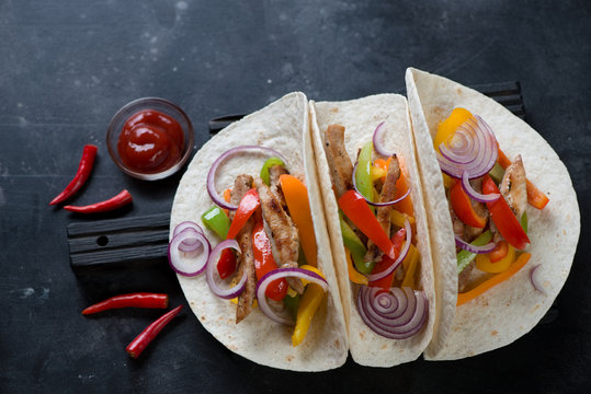 Tortillas filled with freshly made tex-mex pork fajitas. High angle view over dark metal background