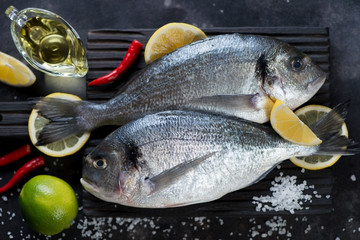 Couple of fresh uncooked seasoned sea breams on a wooden cutting board, close-up, top view