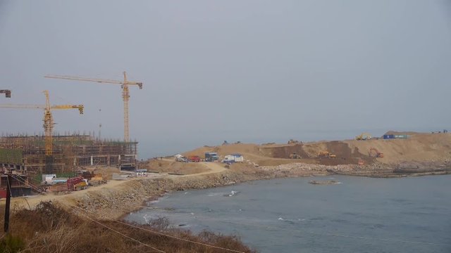 excavator working & dumper truck on construction site near sea.	