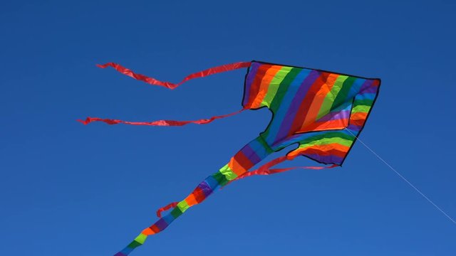 4k Colorful rainbow kite flying against a sunny blue sky handheld