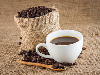 Coffee beans in a sack and fresh coffee in a cup over cloth texture and background