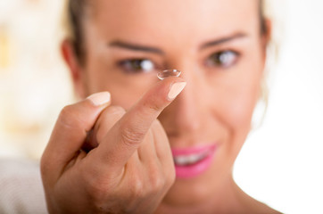 Young woman holding contact lens on finger in front of her face on white background., eyesight and...