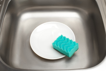 Kitchen sink with clean white plate and green cleaning sponge